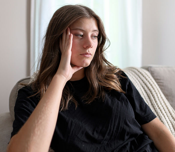 Young woman in a black shirt sitting on a couch, looking pensive and reflecting on toxic in-laws and newborn boundaries. Young woman in a black shirt sitting on a couch, looking pensive and reflecting on toxic in-laws and newborn boundaries.