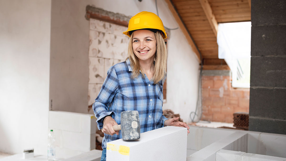 Woman wearing construction helmet and plaid shirt smiling while building wall block, showing land dispute resilience and strength.