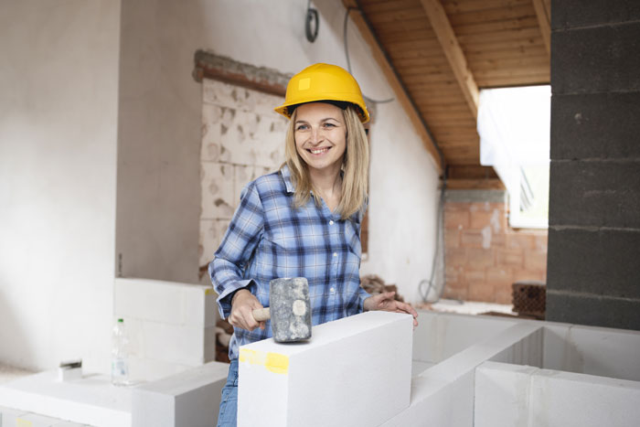 Woman wearing a yellow helmet and plaid shirt working on home construction, defending her land from rude neighbors.