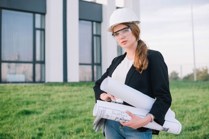 Woman wearing a hard hat and safety glasses holding blueprints, representing lady tolerating rude neighbors over land dispute.