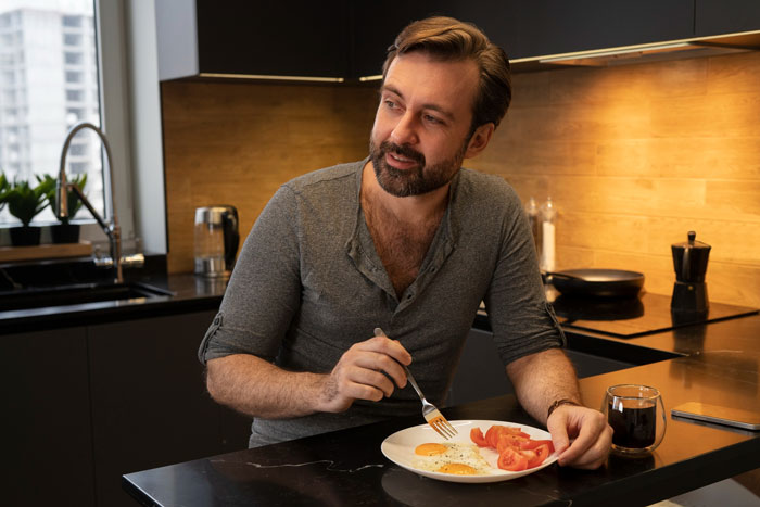 Man eating breakfast alone in kitchen, reflecting on boyfriend mother family expectations and relationships. Man eating breakfast alone in kitchen, reflecting on boyfriend mother family expectations and relationships.