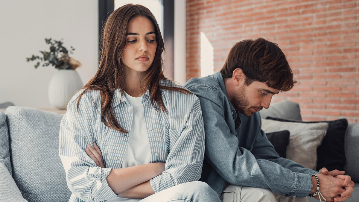 Young couple sitting apart on a couch, looking upset while dealing with boyfriend mother family expectations conflict.