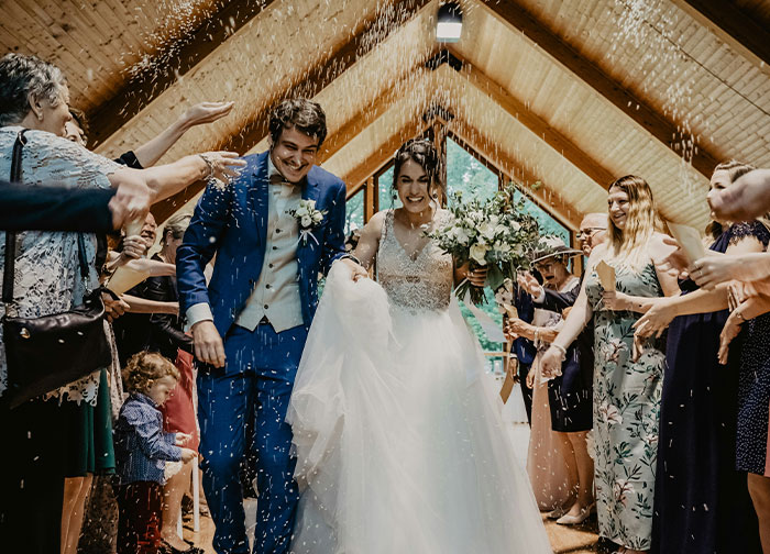 Bride and groom walking down the aisle smiling while guests throw confetti at a wedding ceremony celebration.
