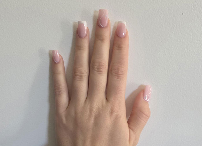 Close-up of a bridesmaid’s hand with freshly done light pink nails before a wedding, showing polished acrylic nails.