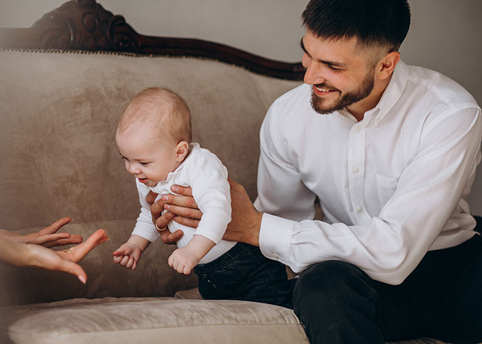 Man holding baby on couch, smiling and interacting, illustrating family dynamics with multiple children and women. Man holding baby on couch, smiling and interacting, illustrating family dynamics with multiple children and women.
