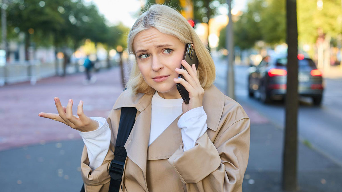 Woman looking frustrated while talking on phone outside, considering calling cops about neighborsu2019 disabled son raiding trash.