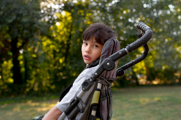 Young disabled boy sitting in wheelchair outdoors with blurred trees in background illustrating neighbor conflict over trash raids Young disabled boy sitting in wheelchair outdoors with blurred trees in background illustrating neighbor conflict over trash raids