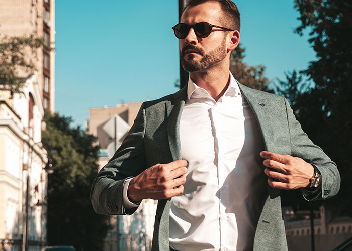 Man in sunglasses adjusting gray blazer outdoors, representing woman calling out brother for having kids with different women. Man in sunglasses adjusting gray blazer outdoors, representing woman calling out brother for having kids with different women.
