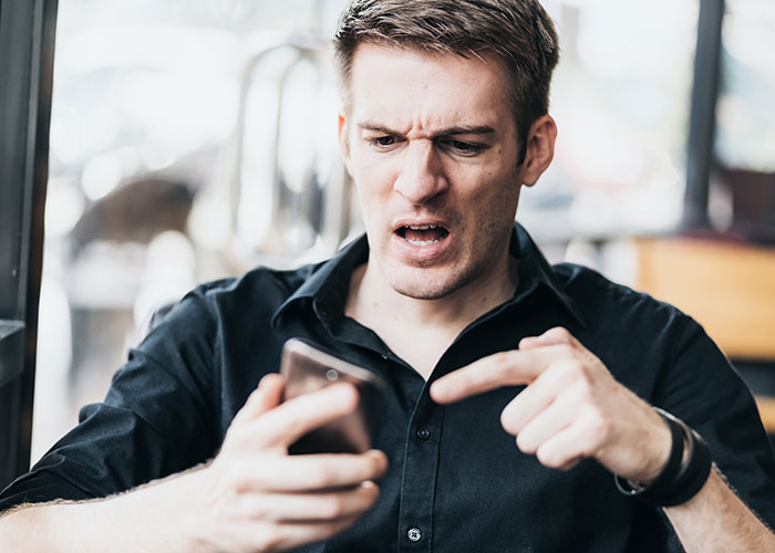 Man in black shirt with angry expression pointing at phone, illustrating monster-in-law conflict and danger to DIL. Man in black shirt with angry expression pointing at phone, illustrating monster-in-law conflict and danger to DIL.