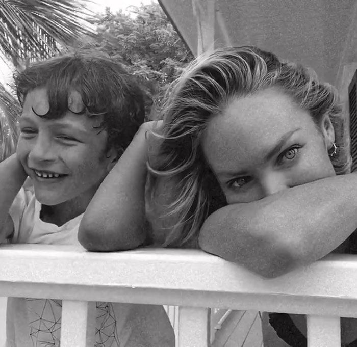 Victoria’s Secret model resting on railing with child, black and white image showing a candid moment outdoors. Victoria’s Secret model resting on railing with child, black and white image showing a candid moment outdoors.
