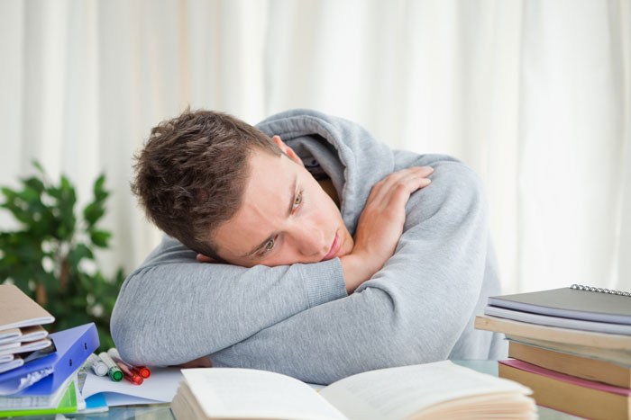 Young man resting his head on his arms at a desk, reflecting the challenges of care brother nocturnal epilepsy.