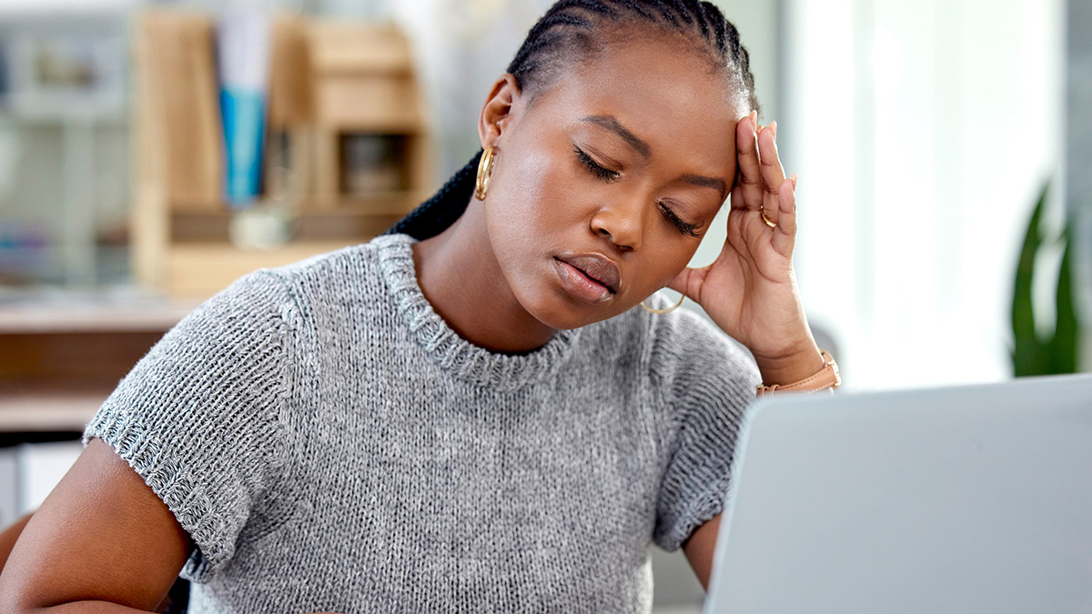 Young woman looking stressed while working on a laptop, illustrating impact of name change on job offers.