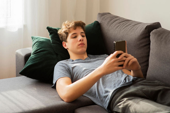 Young man mooching off cousin lounging on couch and using smartphone, avoiding paying $400 rent demand. Young man mooching off cousin lounging on couch and using smartphone, avoiding paying $400 rent demand.