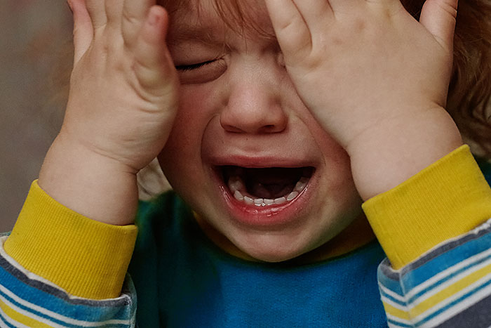 Crying distressed child covering face with hands, representing disruptive kid on a plane upsetting others around. Crying distressed child covering face with hands, representing disruptive kid on a plane upsetting others around.