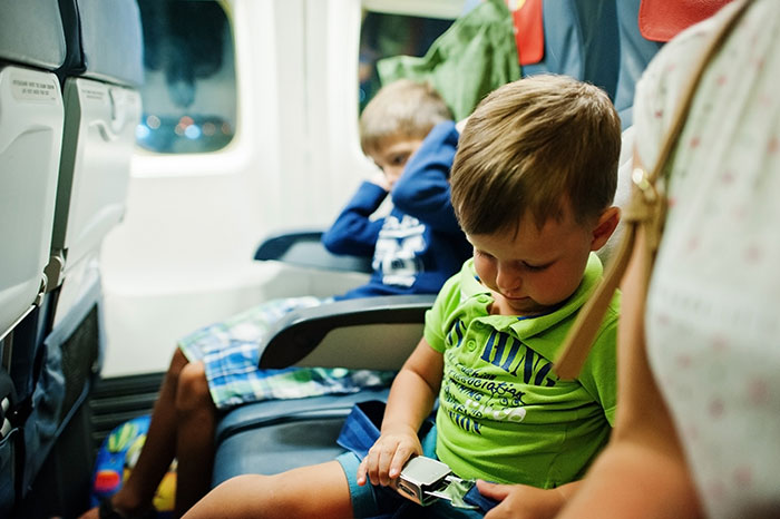 Young disruptive kid on a plane adjusting seatbelt with upset mom and another child in the background Young disruptive kid on a plane adjusting seatbelt with upset mom and another child in the background