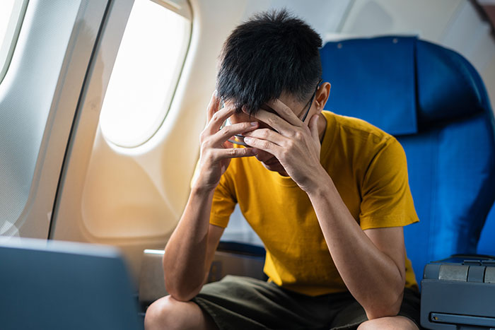 Man on plane covering face in frustration while sitting next to window, upset after telling disruptive kid to shut up. Man on plane covering face in frustration while sitting next to window, upset after telling disruptive kid to shut up.