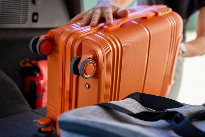 Person packing an orange suitcase in a car trunk, representing travel and positive stereotypes about various countries.