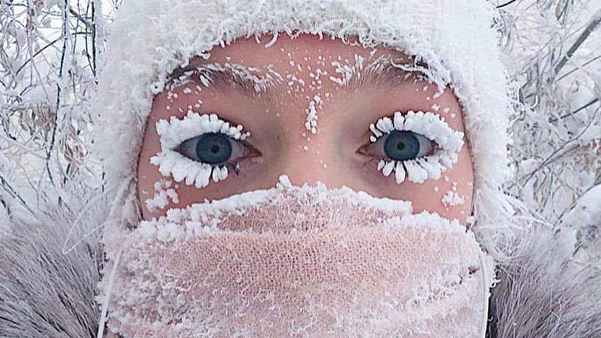 Person living in the coldest city with frost-covered eyelashes and face mask in snowy winter conditions outdoors.