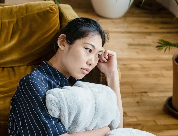 Young woman sitting on couch, holding a pillow and looking thoughtful, reflecting on how to confront parents DNA test. Young woman sitting on couch, holding a pillow and looking thoughtful, reflecting on how to confront parents DNA test.