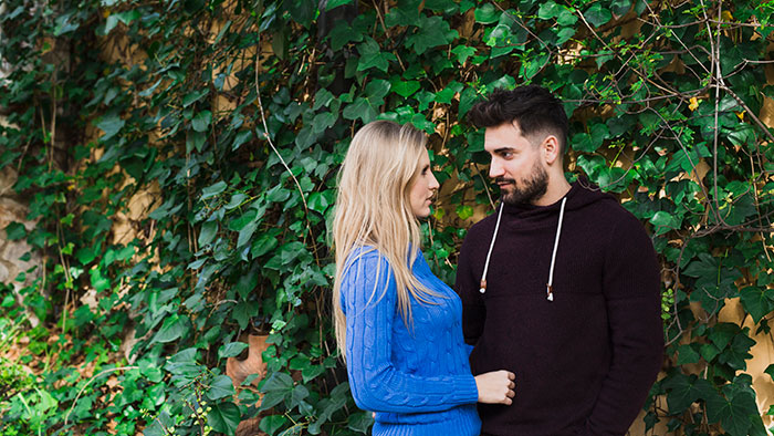 Couple standing close amid green ivy, with the woman looking at the man who appears concerned in a casual setting. Couple standing close amid green ivy, with the woman looking at the man who appears concerned in a casual setting.