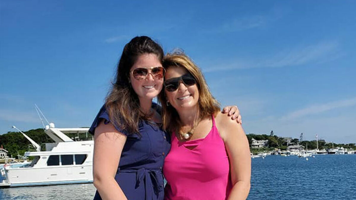Two women wearing sunglasses smiling by the water with a boat in the background, related to woman writes obituary.