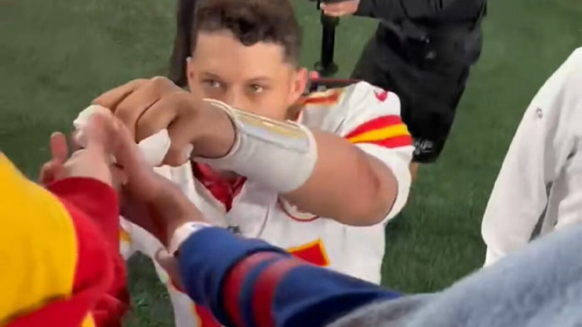 Teen Kansas City football player shaking hands with fans on the field after the game in a white and red jersey.