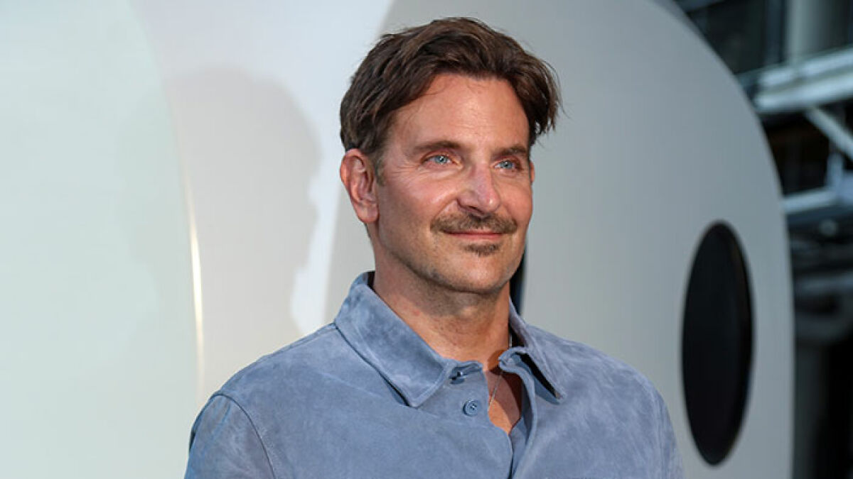 Bradley Cooper posing in a blue jacket with a mustache as plastic surgeons comment on his seemingly new look.