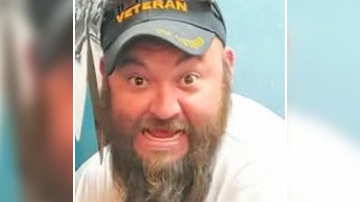 Bearded man wearing a veteran cap with an intense facial expression inside a room.