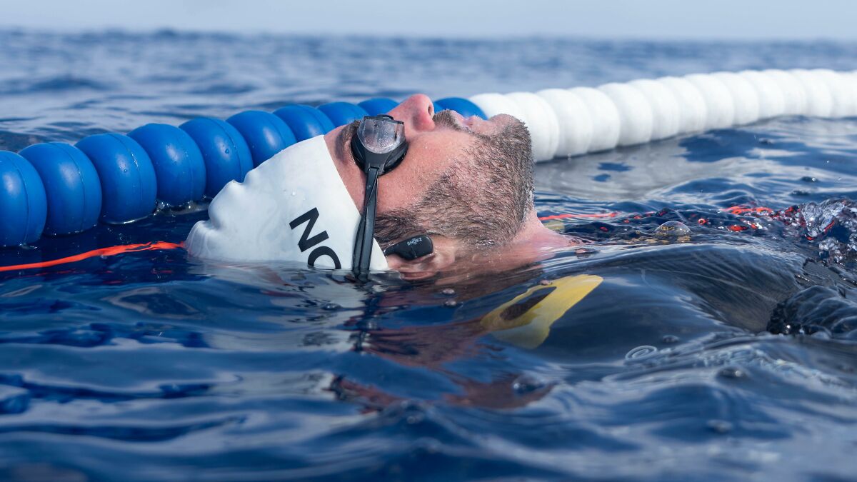 Man wearing swim cap and goggles floating in water near blue and white lane dividers during a swimming session