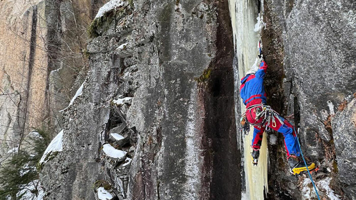 Climber in blue and red gear ascending icy rock face highlighting risks of climbing influencer falls on El Capitan.