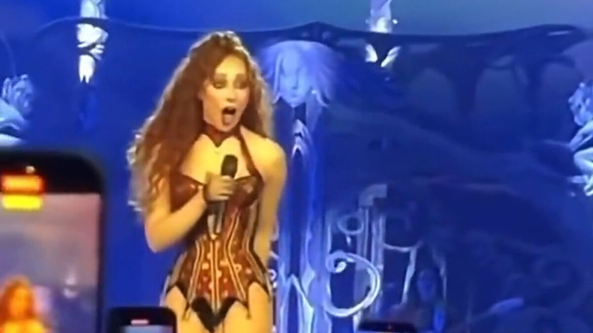 Chappell Roan performing on stage, wearing a revealing corset outfit under dramatic blue lighting.