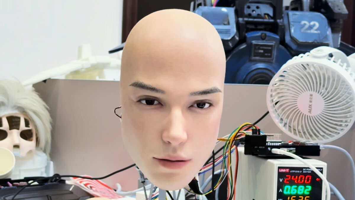 Realistic bald robot head displayed on a desk with wires and electronic equipment, highlighting new tech debate.
