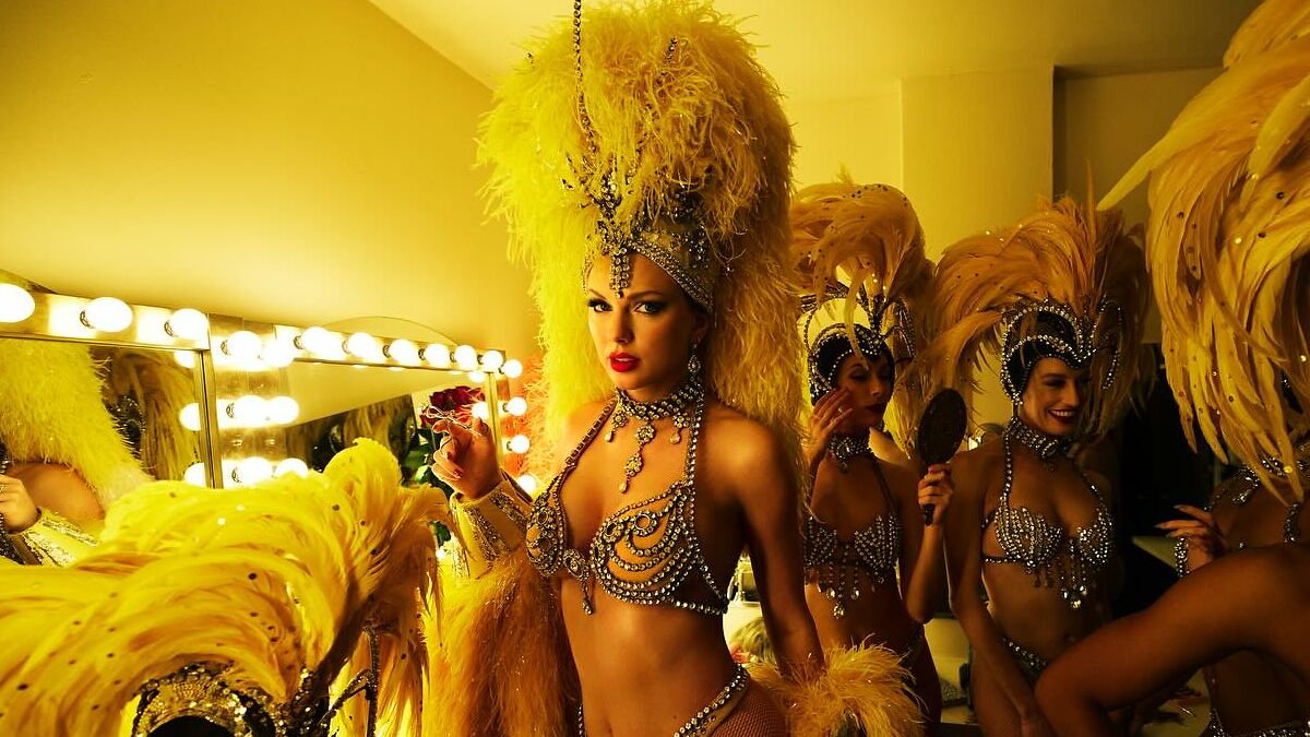 Taylor Swift in elaborate showgirl costume backstage with dancers, highlighting disappointed fans' reaction to new album.