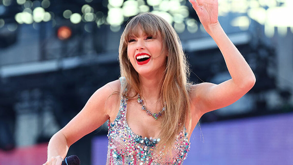 Taylor Swift smiling brightly on stage, wearing a sparkling outfit during a live music performance.