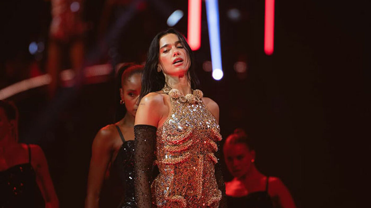 Dua Lipa performing on stage in a glittering outfit with backup dancers during a concert amid massive outrage.