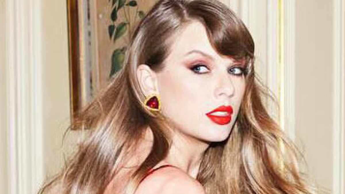 Taylor Swift with red lipstick and earrings, posing indoors, related to album controversy on racism and homophobia allegations.