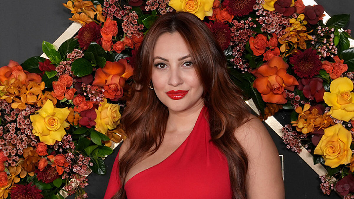 Woman with long brown hair wearing a red dress in front of a colorful floral backdrop about Selena Gomez's kidney donor claims.