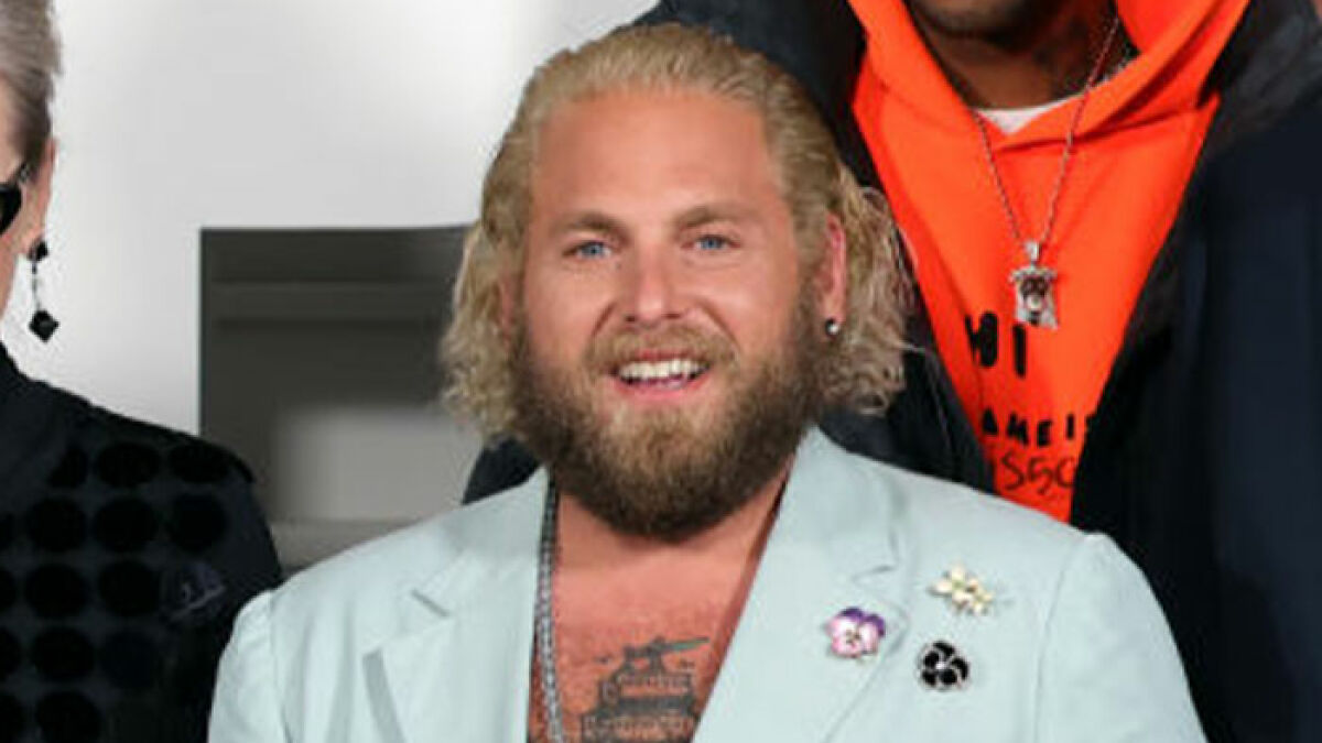 Jonah Hill with blonde hair and beard, wearing a light blue blazer, showcasing his major transformation.