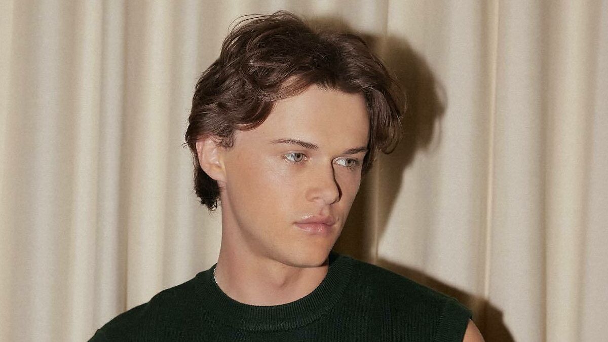 Young man with styled hair wearing a dark green sleeveless top posing indoors for most handsome man in the world 2025.