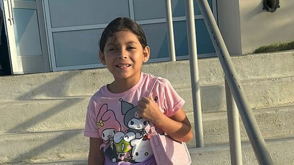 Young girl outside school with a pink shirt, amid massive outrage over school bullies cutting her hair story.