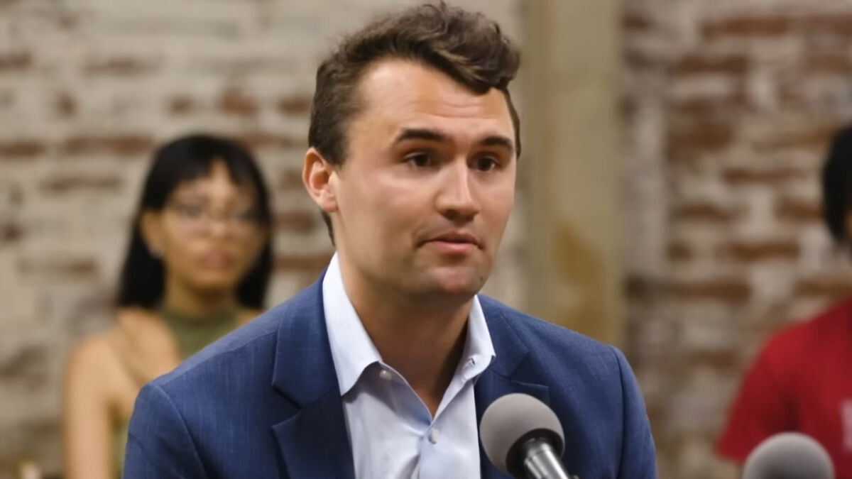 Man in blue suit speaking into microphone during video about Life of Charlie Kirk homework assignment outrage.