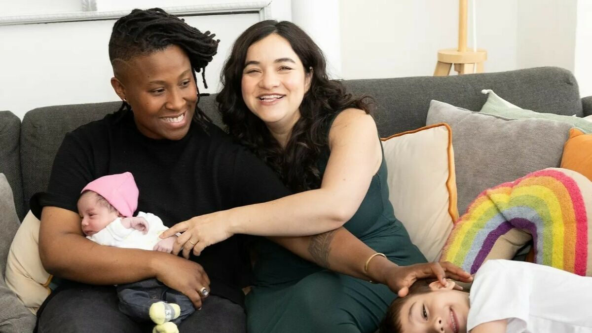 Two women smiling on a couch with their children, representing female professor lifestyle and family choices.