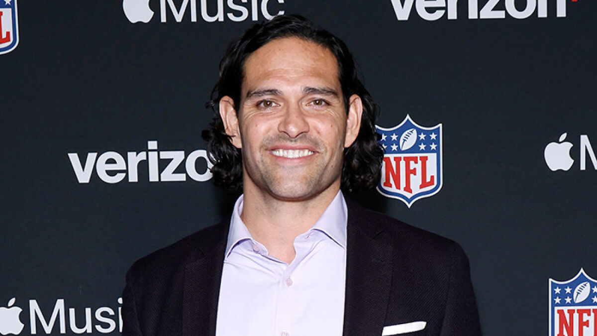 Mark Sanchez smiling at NFL event with Verizon and Apple Music logos on the backdrop behind him.
