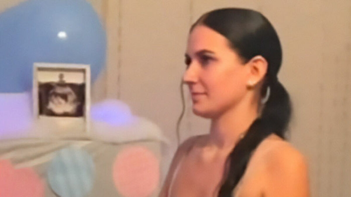 Woman with long dark hair in a ponytail at a gender reveal party with blue and pink decorations in background.