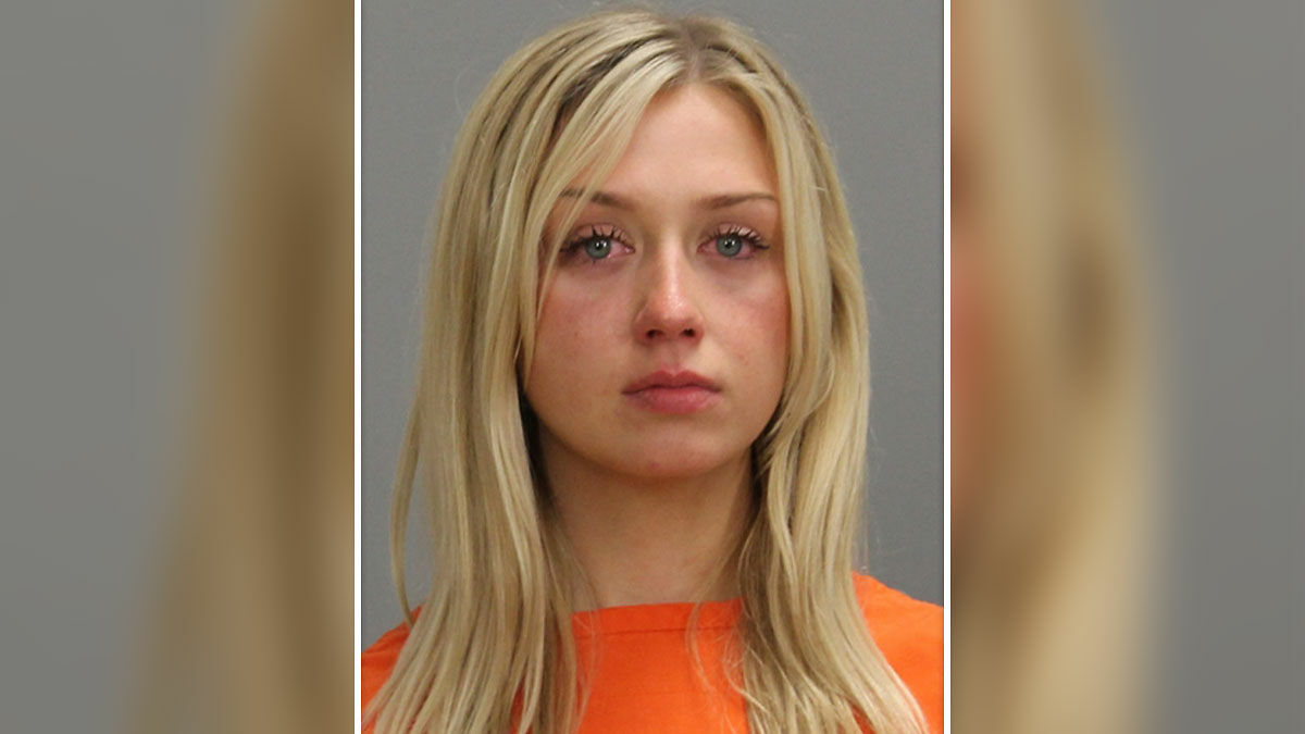 Student caught in Olive Garden hoax wearing orange jumpsuit with a serious expression against a gray background.