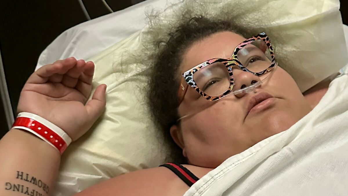 Plus-size activist lying in bed with oxygen tube and patterned glasses, resting after alleged run-in with the law.