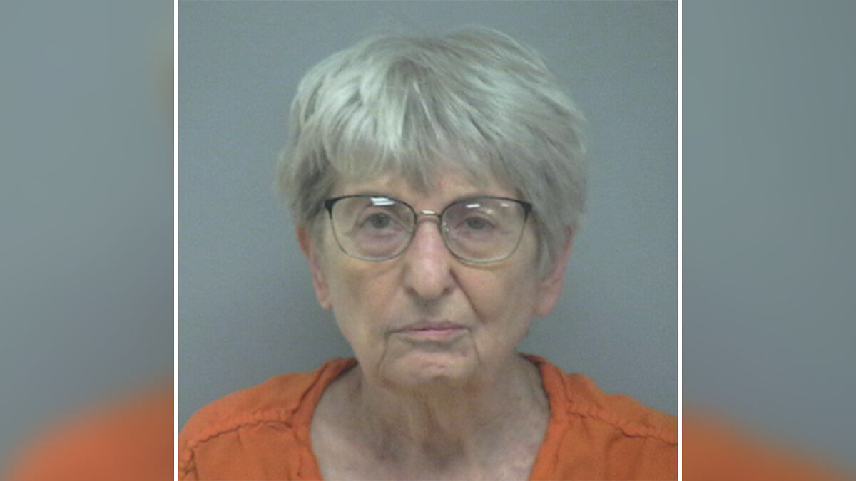 82-year-old woman in orange prison clothing, wearing glasses, photographed for fatal attack on her husband case.