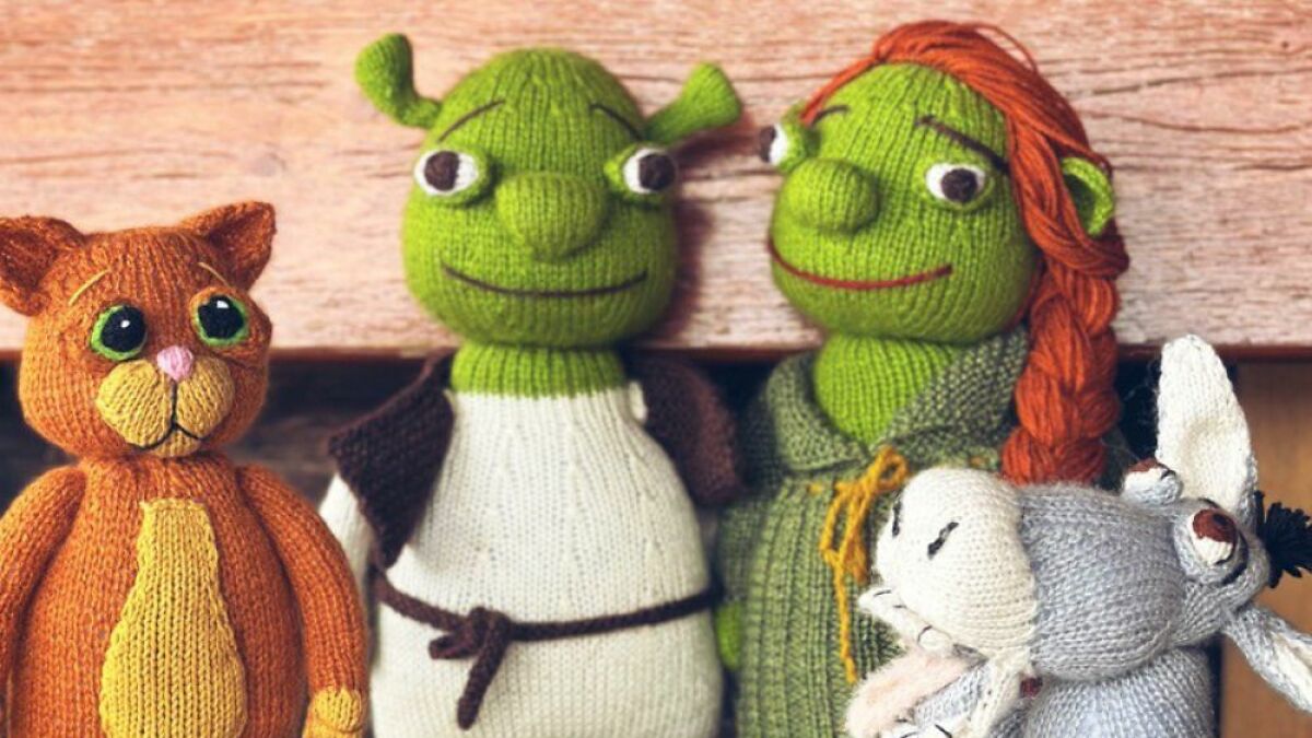 Knitted Puss In Boots cat doll next to green knitted characters and a gray knitted donkey on a wooden background.