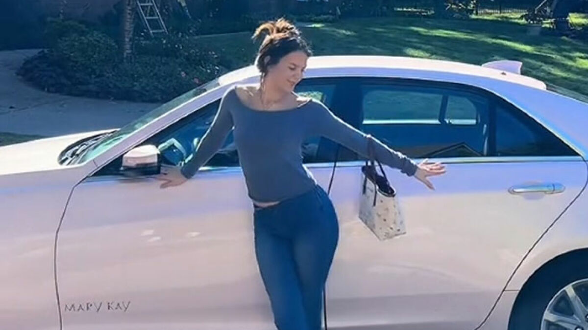 Woman posing over a Mary Kay Cadillac car in a sunny outdoor setting, sparking viral TikTok reactions and dealership calls.