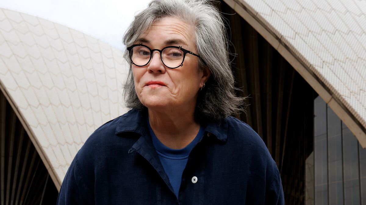 Rosie O'Donnell wearing glasses and a dark blue shirt, posing outdoors with an expressive look, Keanu Reeves controversy.